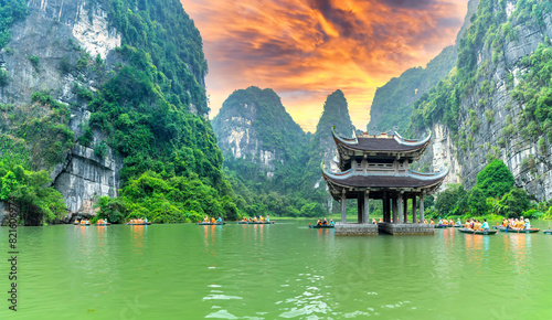 Ninh Binh, Vietnam - April 5th, 2024: Tourists float by boat on the river of the Tam Coc National Park Sightseeing tour to grottoes with sunset sky, Ninh Binh, Vietnam.