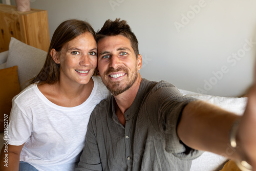Young couple taking selfie relaxing sitting on the sofa looking at camera.