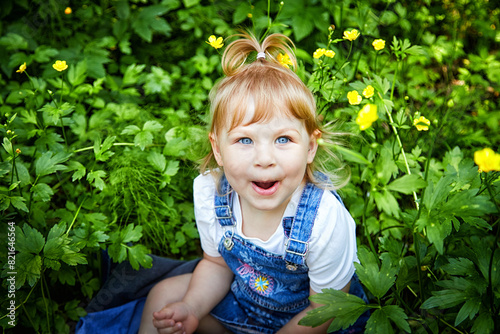 Joyful Toddler Among Spring Flowers. A toddler with bright blue eyes sits among blooming yellow flowers, smiling. A healthy child in the fresh air. Good ecology