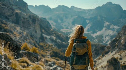 In the midst of rugged mountain scenery, a resilient backpacking woman blazes her own trail, her backpack packed with essentials for the journey ahead