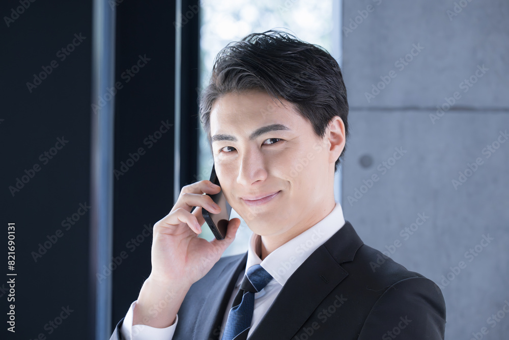 Exec. male businessman in suit smiling at window making a phone call (talking), looking at camera. Exec. male businessman in suit smiling at window making a phone call (talking), looking at camera.