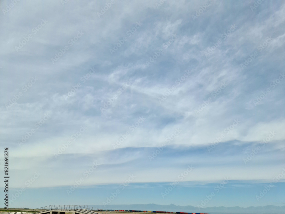 Obraz premium The sky is evenly filled with clouds stretching to the horizon, where a freight train is traveling.