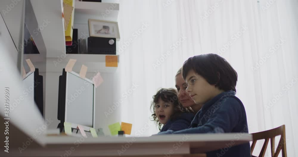 A mother helps her child with computer work at home, both focused on the task at hand in a well-lit room. A mother helps her child with computer work at home, both focused on the task at hand in a well-lit room.