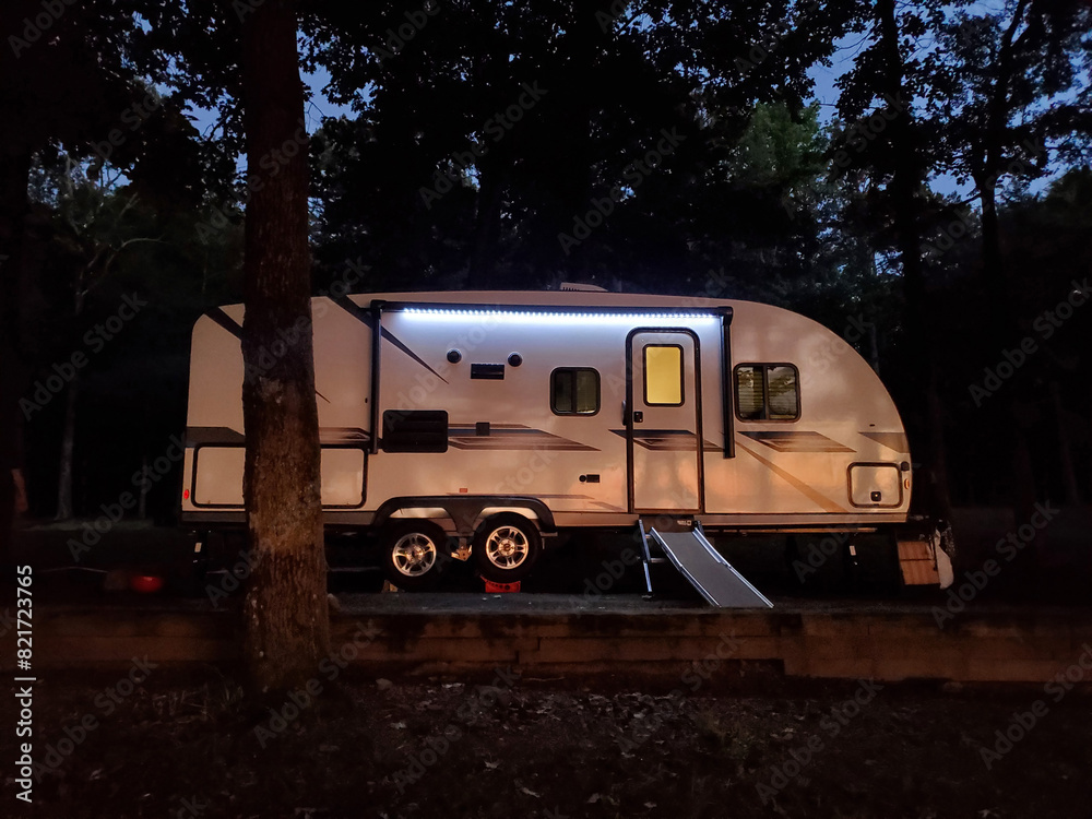 Illuminated camper trailer parked in forest at night. Illuminated camper trailer parked in forest at night.