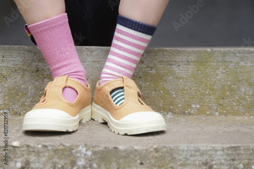 Kid wears different pair of socks. Child foots in mismatched socks standing outdoor. Down syndrome awareness concept, odd socks day, anti-bullying week.