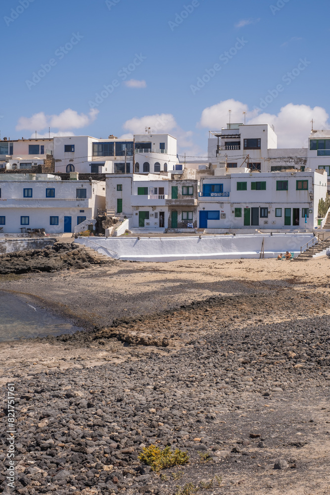 Bay and typical houses of the fishing village of Caleta de Caballo. White houses. Rock coast in the foreground. Turquoise water. Calm sea. Caleta de Caballo, Lanzarote, Canary Islands, Spain. Bay and typical houses of the fishing village of Caleta de Caballo. White houses. Rock coast in the foreground. Turquoise water. Calm sea. Caleta de Caballo, Lanzarote, Canary Islands, Spain.