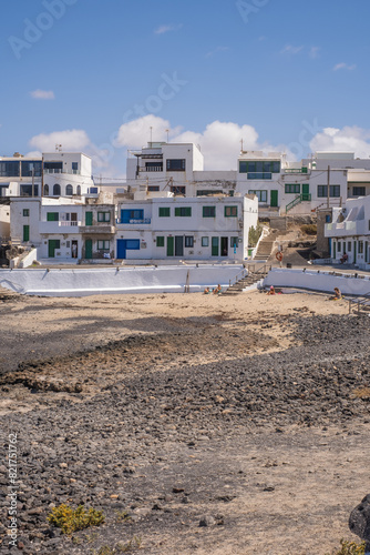 Bay and typical houses of the fishing village of Caleta de Caballo. White houses. Rock coast in the foreground. Turquoise water. Calm sea. Caleta de Caballo, Lanzarote, Canary Islands, Spain. © Jess