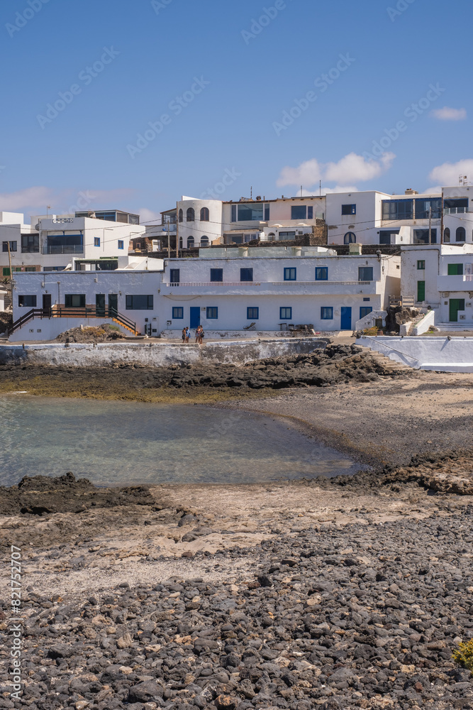 Bay and typical houses of the fishing village of Caleta de Caballo. White houses. Rock coast in the foreground. Turquoise water. Calm sea. Caleta de Caballo, Lanzarote, Canary Islands, Spain Bay and typical houses of the fishing village of Caleta de Caballo. White houses. Rock coast in the foreground. Turquoise water. Calm sea. Caleta de Caballo, Lanzarote, Canary Islands, Spain