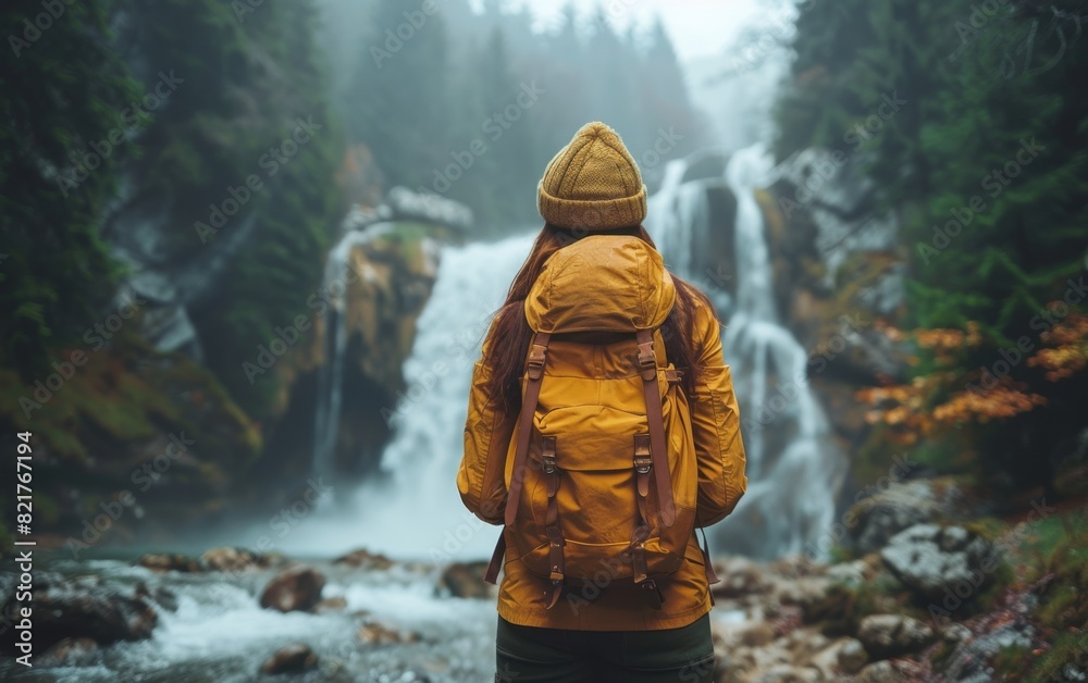 A mixed race adult wearing a yellow jacket and brown backpack standing in an outdoor setting A mixed race adult wearing a yellow jacket and brown backpack standing in an outdoor setting