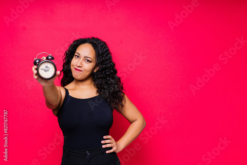 Smiling young african american woman posing isolated on red background with clock