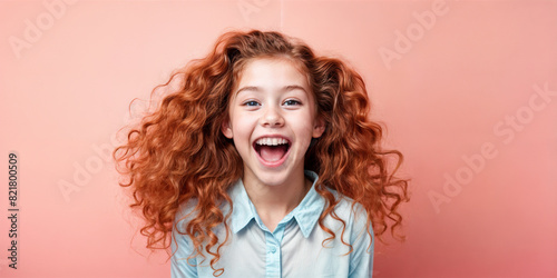 Cute young child Little girl smiles. Emotion and child development. Little girl smiles while red hair. A young girl with curly hair is smiling and laughing while wearing a shirt.