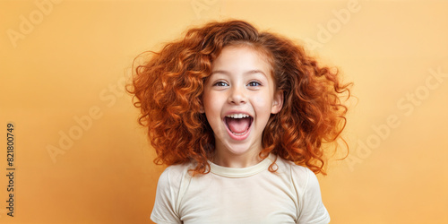 Cute young child Little girl smiles. Emotion and child development. Little girl smiles while red hair. A young girl with curly hair is smiling and laughing while wearing a shirt.