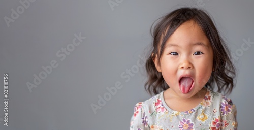 Cute Asian child girl show tongue isolated on grey background. photo