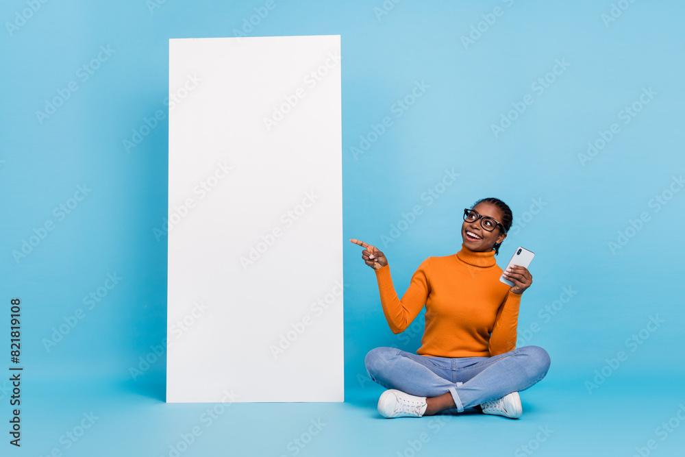 Portrait of beautiful trendy cheery girl using device showing copy blank empty space poster isolated over blue color background Portrait of beautiful trendy cheery girl using device showing copy blank empty space poster isolated over blue color background