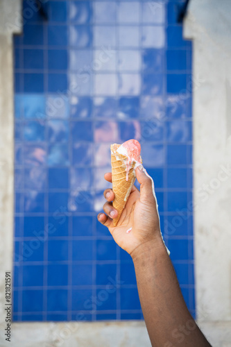 Man holding melting Ice cream cone in front of blue tile wall