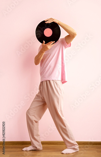 Man wears pink clothes and holds vinyl record near his face dances against pink wall.