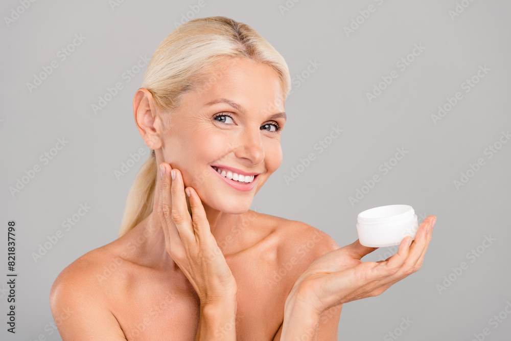 Photo of adorable pretty old woman naked shoulders smiling applying cheeks face cream empty space isolated grey color background Photo of adorable pretty old woman naked shoulders smiling applying cheeks face cream empty space isolated grey color background