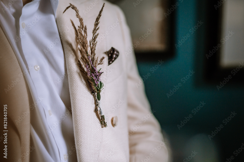Obraz premium Riga, Latvia, - August 26, 2024 - A close-up of a beige suit with a boutonniere made of dried grasses and small flowers pinned to the lapel, showcasing elegance and style.