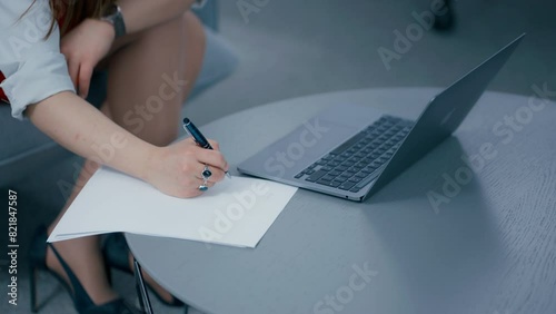 Close up of a woman's hand working writing information down on the paper in slow motion. Secretary wearing red skirt and white shirt, sitting on the couch. photo