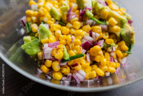  vibrant colors of a summer salad featuring corn, red onion, and avocado, drizzled with lime dressing, presented in a glass bowl in this closeup