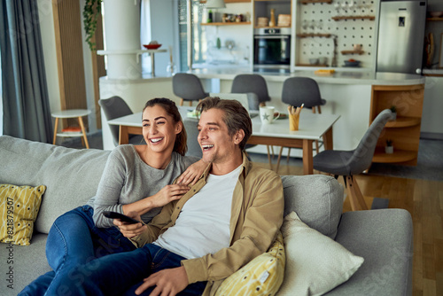 A happy couple sitting on a couch in their living room and watching TV