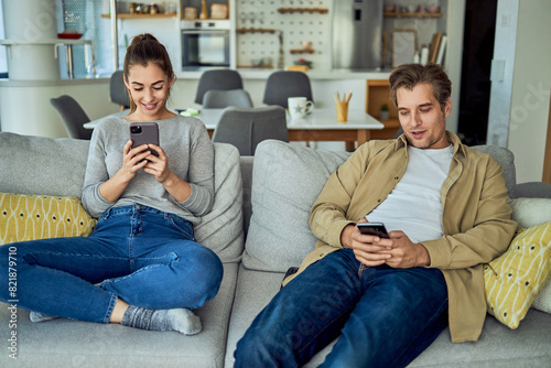 A happy couple using their phones and sitting on the couch in the living room
