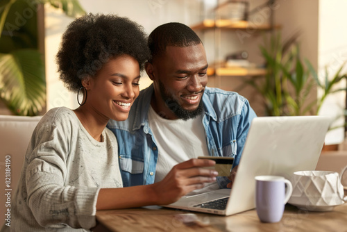 A happy young couple making a credit card payment on a laptop together at home.