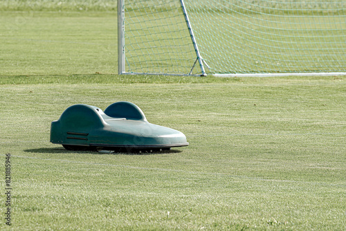 An autonomous battery lawn mower cuts the grass on an amateur football field.