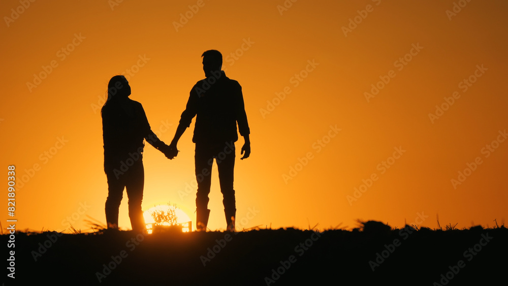 Silhouettes of a romantic couple. Holding hands and standing against the backdrop of a beautiful sunset Silhouettes of a romantic couple. Holding hands and standing against the backdrop of a beautiful sunset