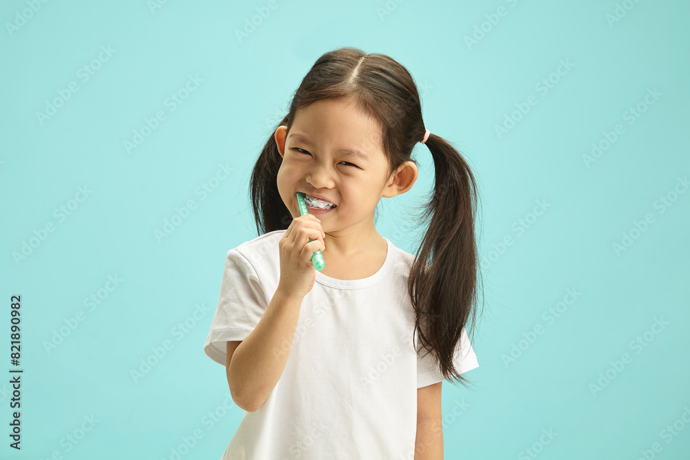 Face of Japanese child girl cleaning mouth with a brush for morning routine and oral self care. Happy asian ethnicity kid using toothbrush standing over blue isolated background with free copy space. Face of Japanese child girl cleaning mouth with a brush for morning routine and oral self care. Happy asian ethnicity kid using toothbrush standing over blue isolated background with free copy space.