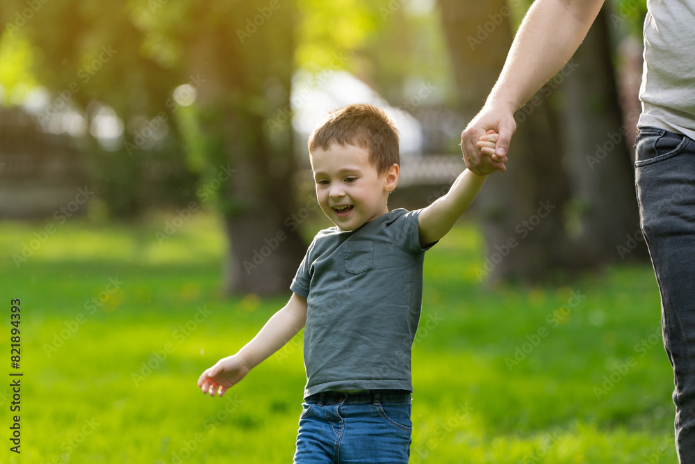 Happy three year old toddler boy walks hand in hand with dad in the park on a sunny spring day. The concept of family walks and spending time together.fathe Happy three year old toddler boy walks hand in hand with dad in the park on a sunny spring day. The concept of family walks and spending time together.fathe