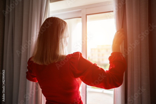 Woman opening curtains in the room at sunny morning.