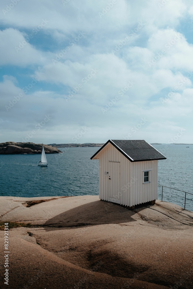 White building on the shore with a sailboat sailing in the sea in the background. White building on the shore with a sailboat sailing in the sea in the background.