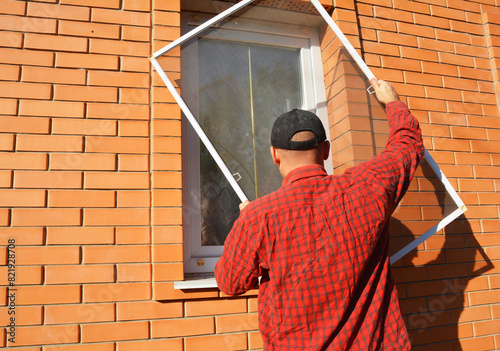 A man installs a mosquito net on a window of brick house outdoor. Mosquito screen installation
