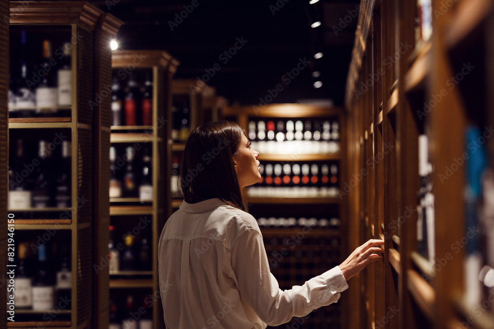 Caucasian female waiter takes wine from shelf in cellar. Sommelier choose alcohol drink for restaurant visitor.