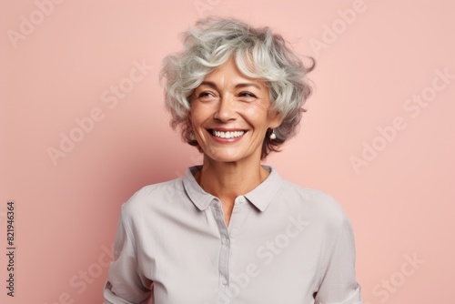 Portrait of a happy woman in her 60s smiling at the camera while standing against solid pastel color wall