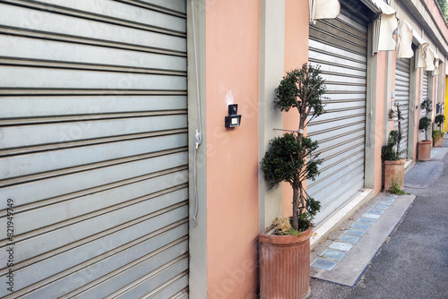 Closed Metal Roll-Up Garage Doors with Potted Trees on Street Sidewalk