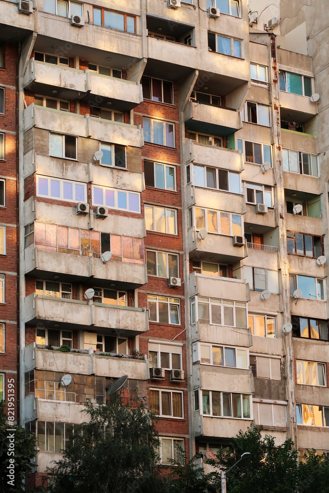 Obraz premium Orange, yellow, pink reflection of the sunset in the many windows of a concrete, socialist, brutalist panel, multi-story, high-rise, apartment block, building, Sofia, Bulgaria