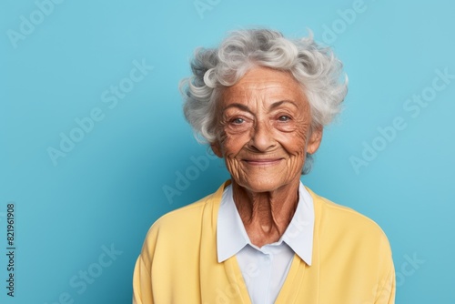 Portrait of a smiling elderly 100 year old woman smiling at the camera in front of solid pastel color wall