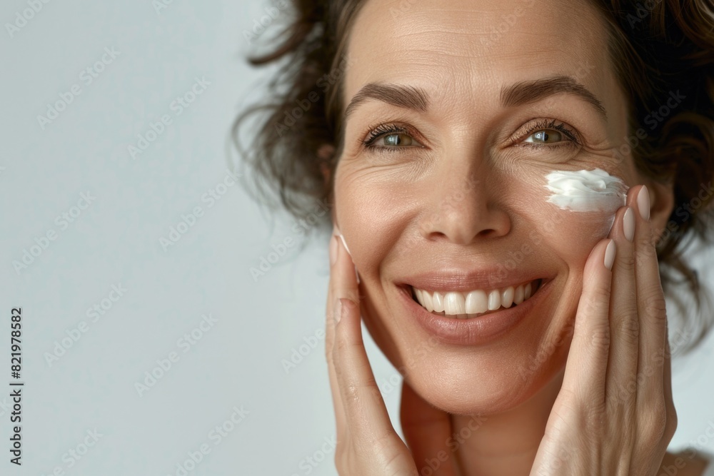 A woman smiling while applying cream to her face. Suitable for beauty and skincare concepts A woman smiling while applying cream to her face. Suitable for beauty and skincare concepts