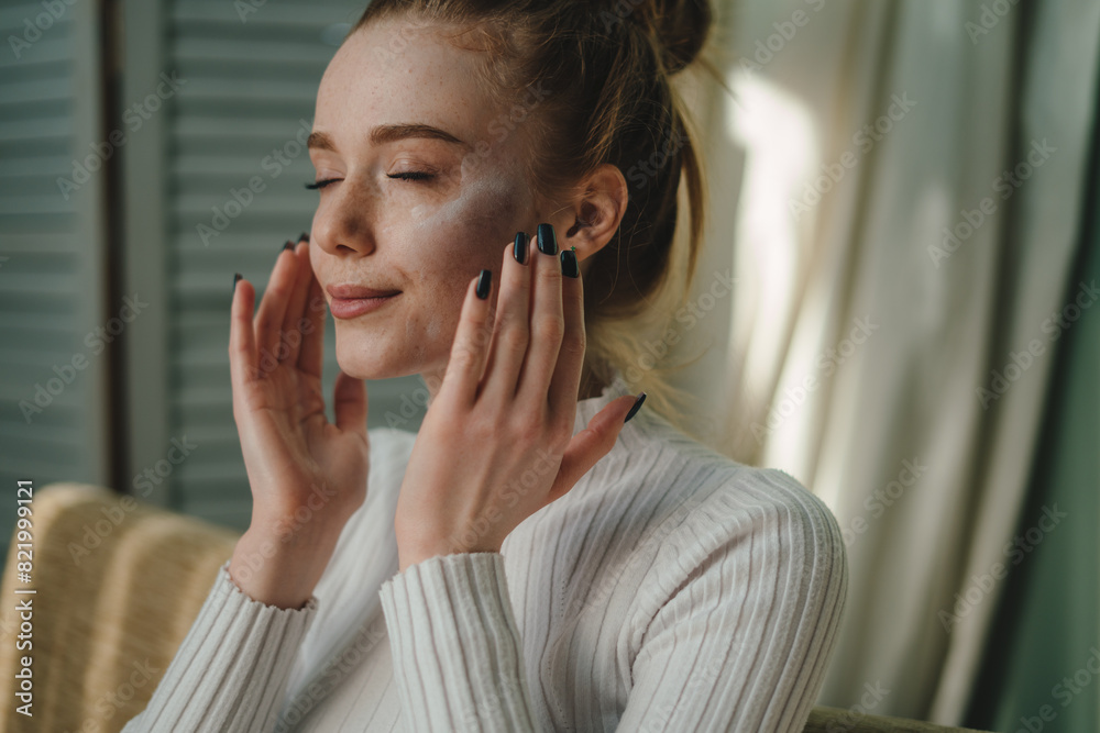Portrait of a beauty ginger woman moisturizing her face skin rubbing with fingers sitting on sofa at home. Portrait of a beauty ginger woman moisturizing her face skin rubbing with fingers sitting on sofa at home.