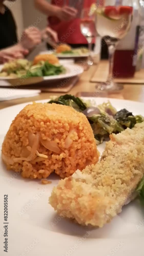 Closeup vertical shot of breaded fish fillet with seasoned greens and tomato rice in white plate Closeup vertical shot of breaded fish fillet with seasoned greens and tomato rice in white plate