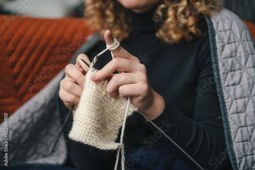 Hands of an unrecognizable young woman knitting product from white woolen thread. Young woman knitting wool product.