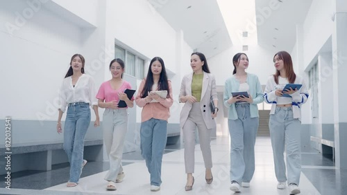 A group of women are walking down a hallway, each holding a tablet. Scene is casual and relaxed, as the women are not wearing formal attire and are simply walking and using their tablets