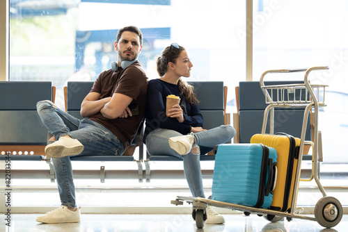 couple arguing about their vacation. Couple fights at the airport while waiting for their plane. Couple turn their backs on each other angry. Young tourists arguing because of forgotten things.