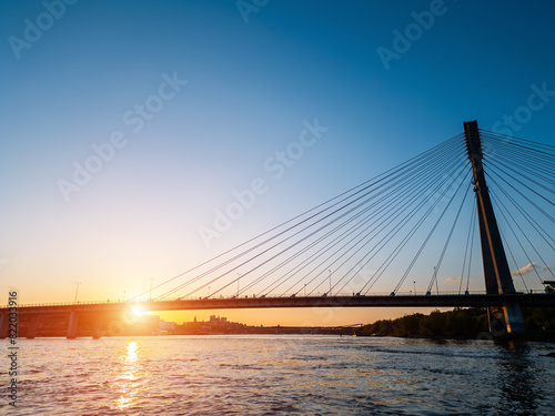modern cable bridge over Vistula river at sunset, contemporary structures of Warsaw, blue sky on background