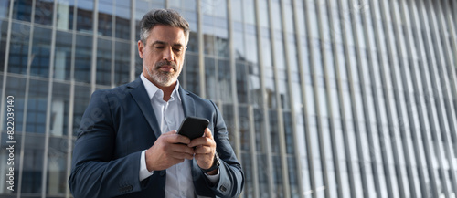 Banner with copy space mature hispanic senior business man using smartphone cellphone at office building. Focused serious latin middle age entrepreneur businessman holding mobile cell phone for work