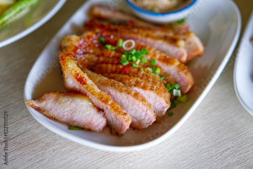 Grilled sliced pig neck on a white plate with natural light, popular grilled meat of Thailand menu.