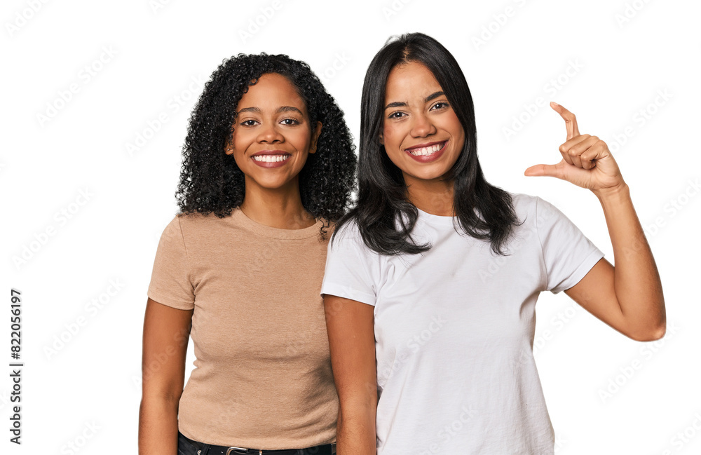 Young Latin friends in studio holding something little with forefingers, smiling and confident. Young Latin friends in studio holding something little with forefingers, smiling and confident.