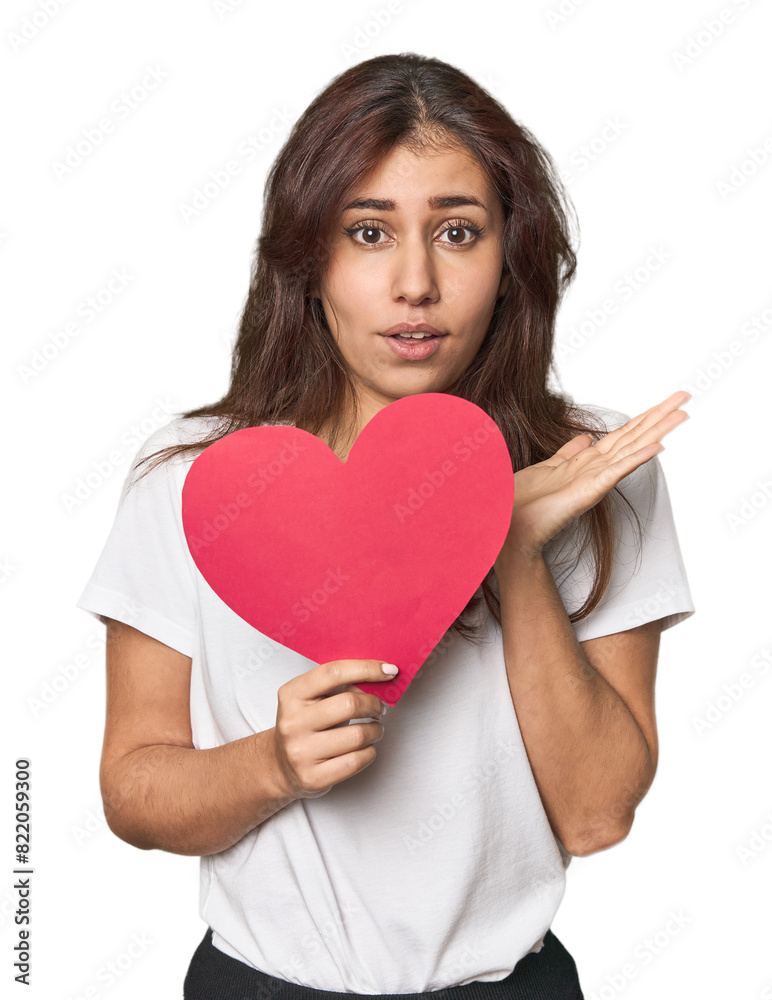 Middle Eastern woman holding paper heart surprised and shocked. Middle Eastern woman holding paper heart surprised and shocked.